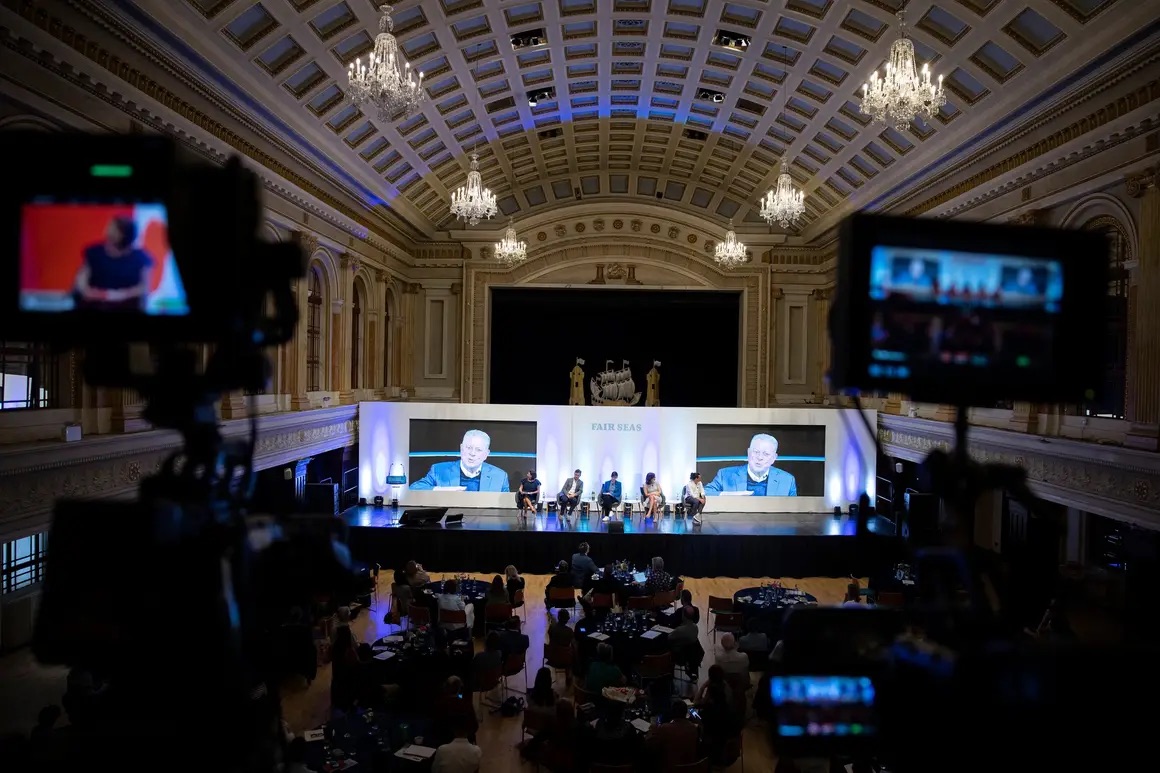 TV cameras and monitors are filming a speaker on the main stage of the Concert Hall