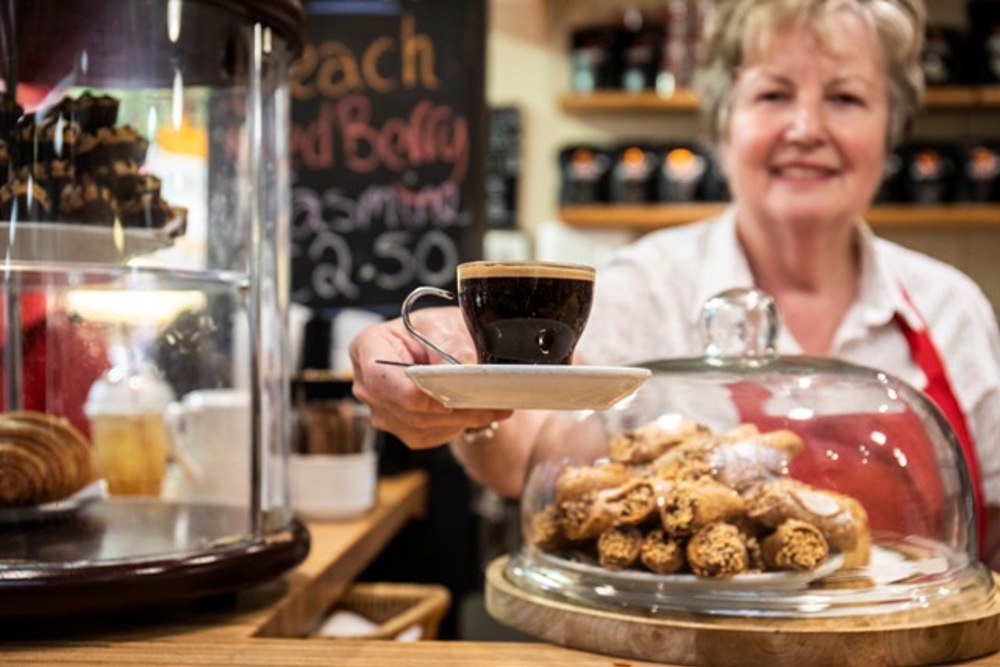 Empemployee handing coffee over scone display towards camera